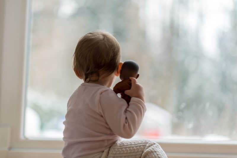 Baby with a doll looking out a window
